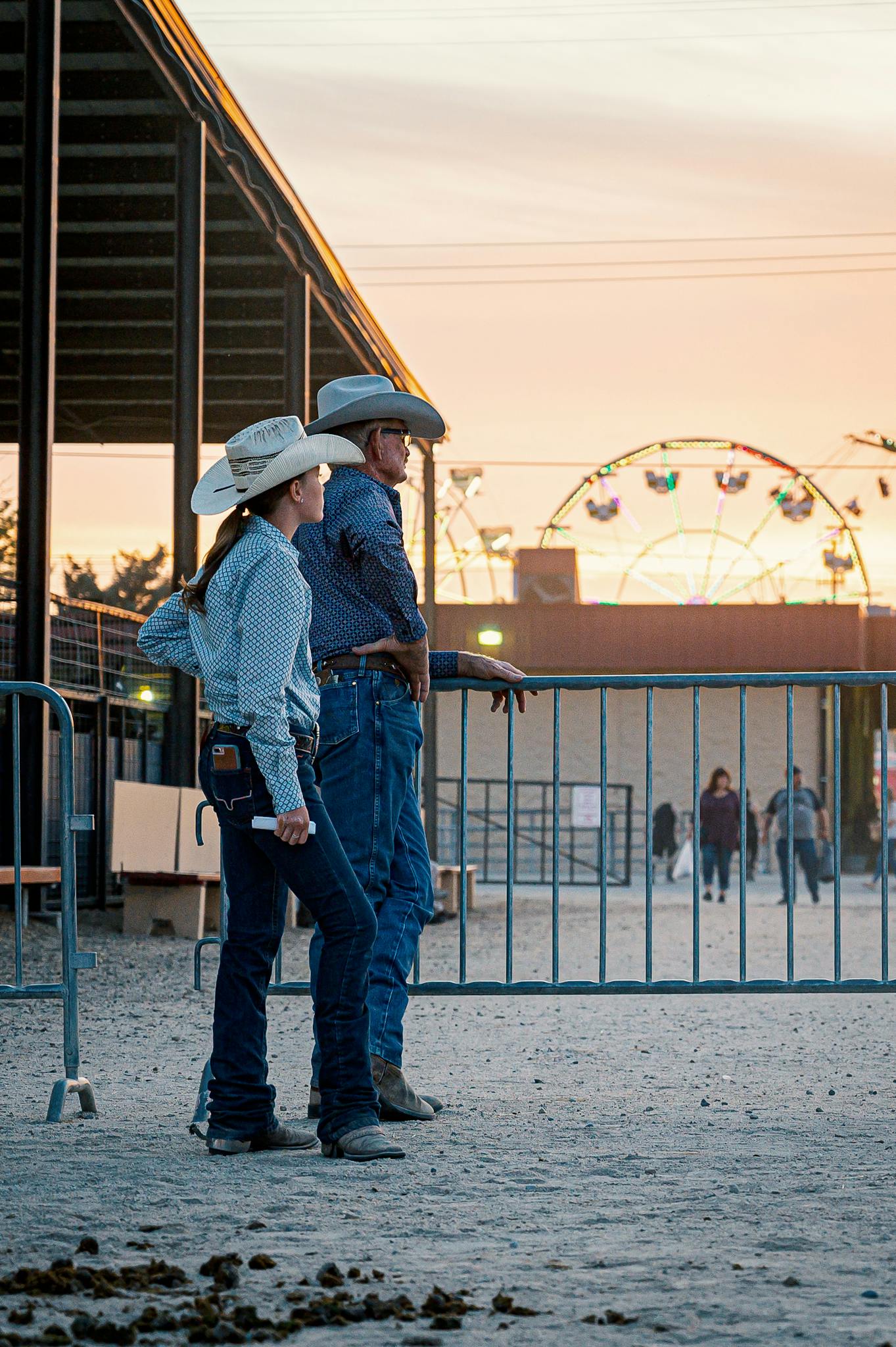 Two cowboys stand outdoors at sunset, capturing a classic western lifestyle moment at a fairground.